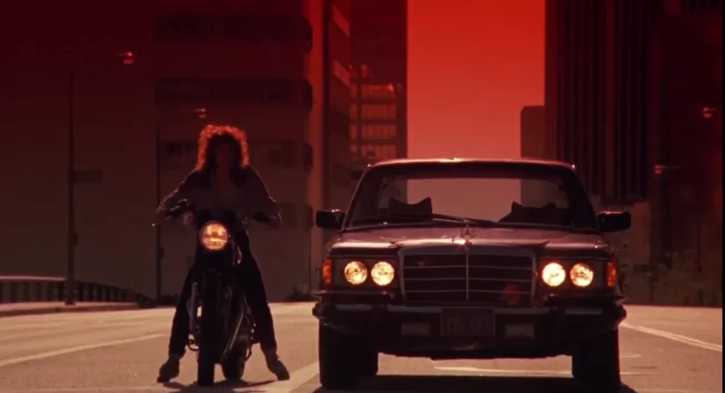 Motorcycle rider next to car at sunset.